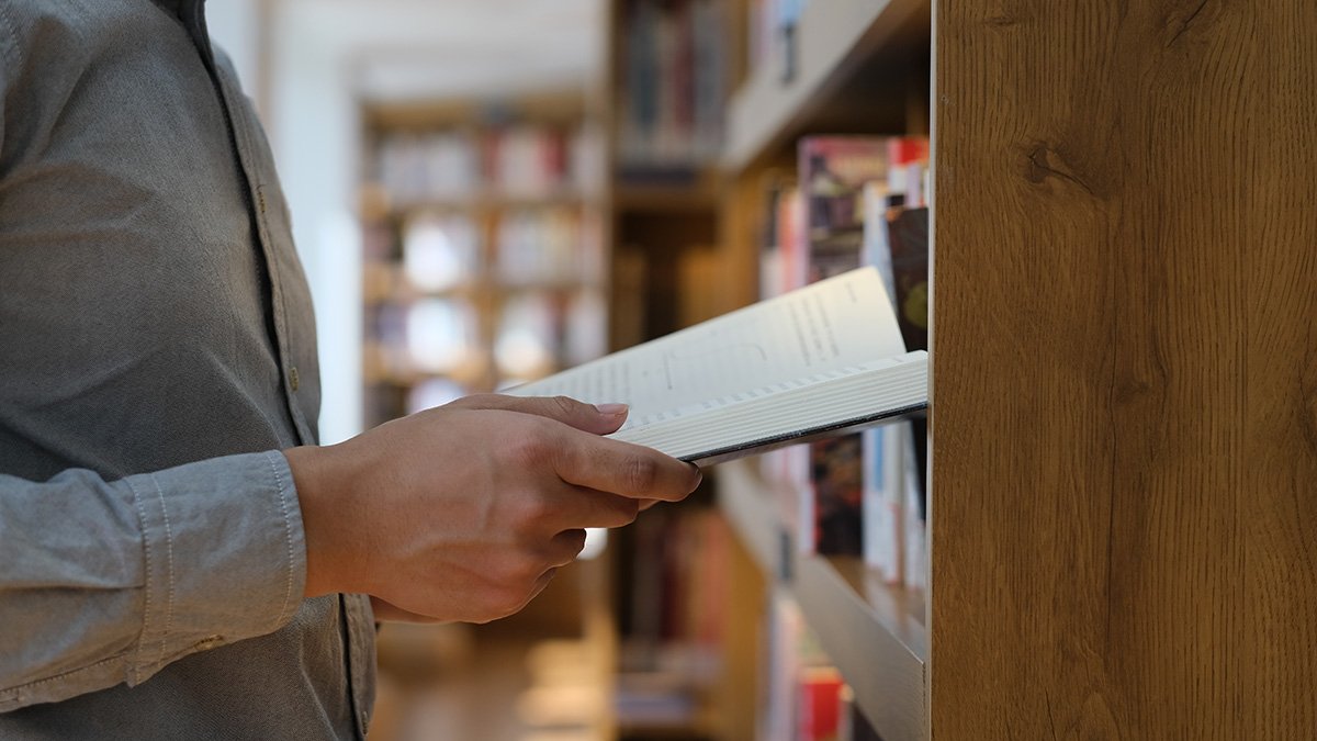 Man bland hyllor håller i en bok