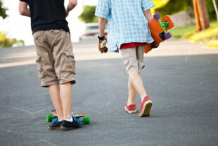 Två barn, utan att huvudena syns, i shorts och med skateboards på asfalt.