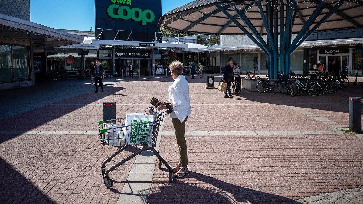Kvinna står med kundvagn på parkering, skylt med ordet Coop i bakgrunden