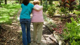 två kvinnor går bredvid varandra i trädgård, en yngre och en äldre