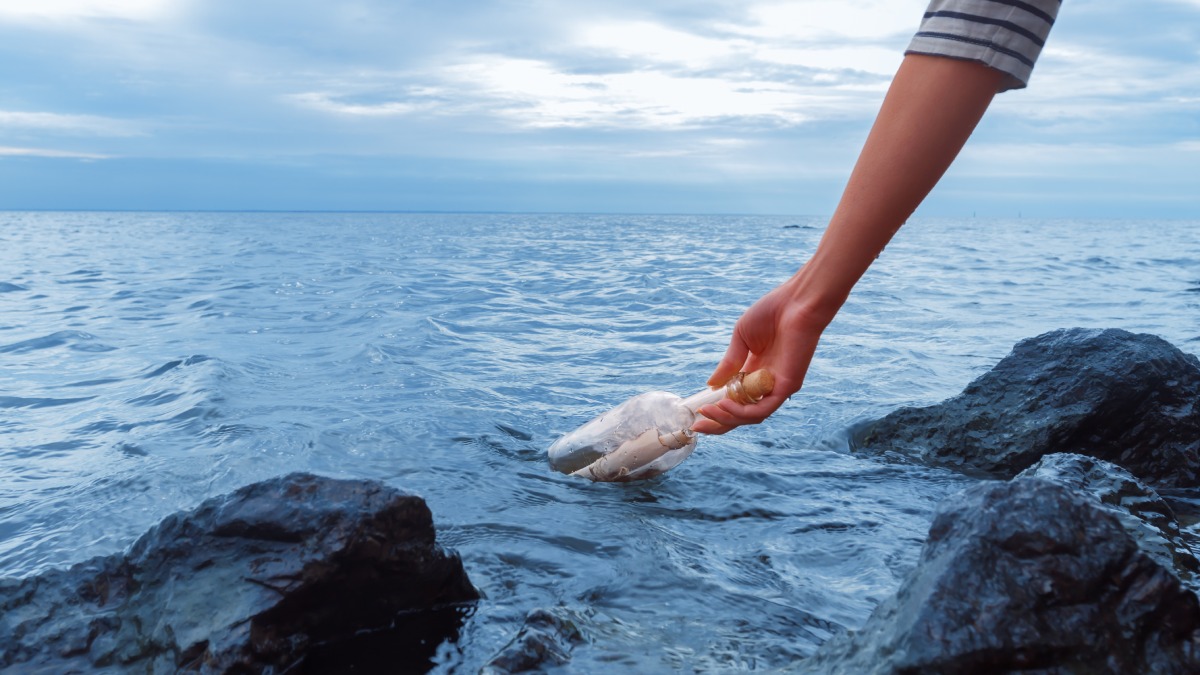 En arm fiskar upp en flaska ur havet.