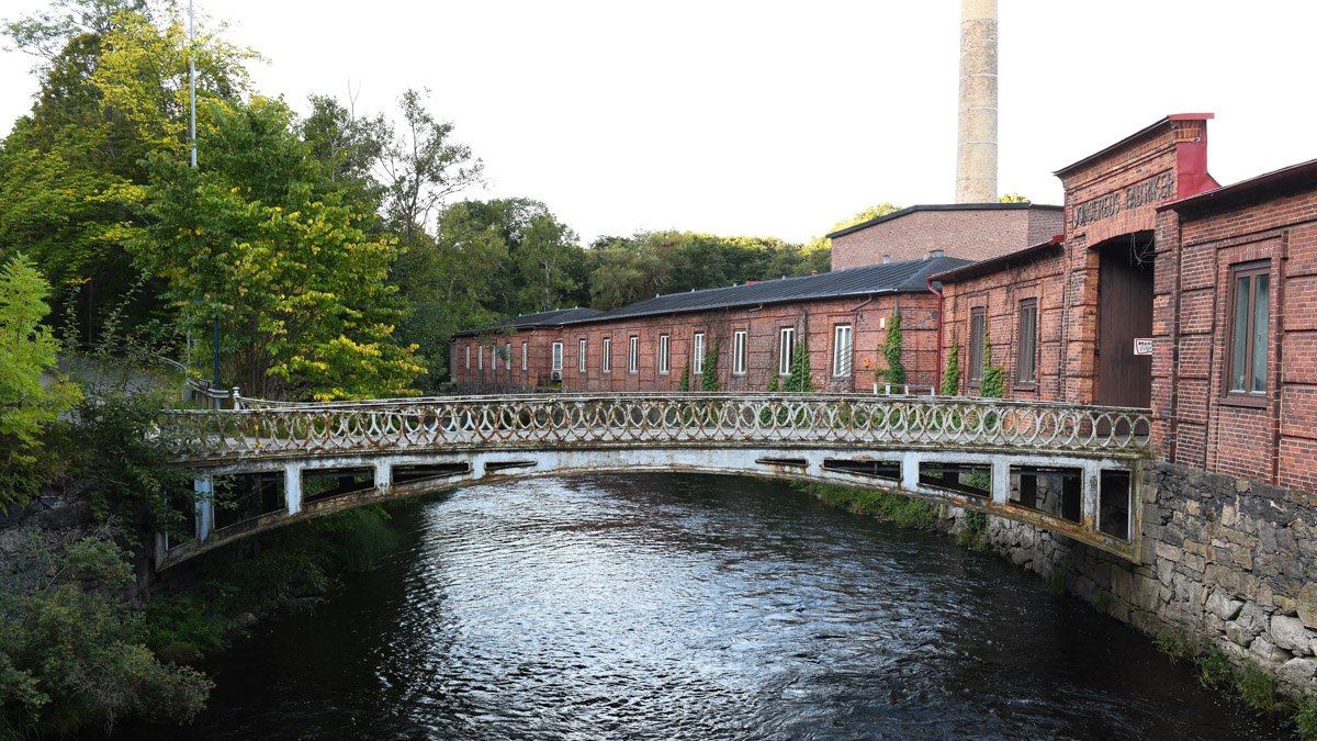 Rostig gjutjärnsbro med flagnande färg. Bron leder in till Jonseredsfabrikens gamla entré.