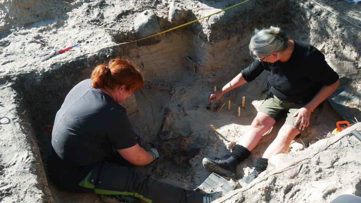 Två personer gräver i ett fyrkantigt hål i sanden.