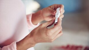 Kvinna med rosa tröja håller graviditetstest i händerna.