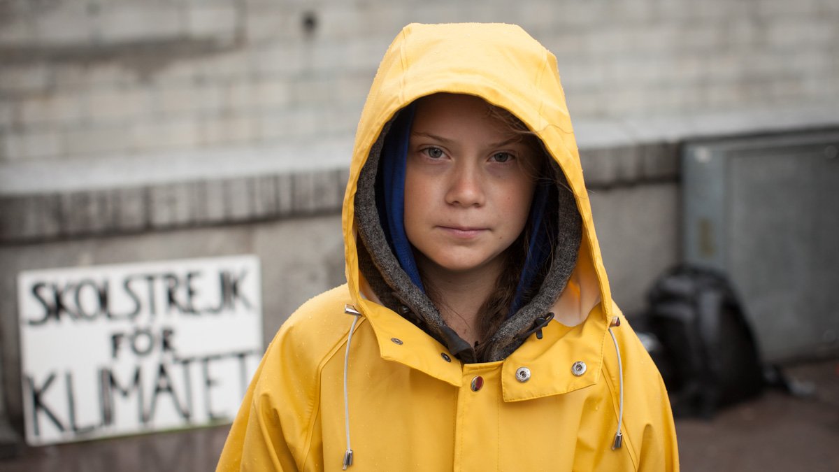 Greta Thunberg, klädd i gul regnjacka, står med en skylt med budskapet ” Skolstrejk för klimatet” utanför Sveriges riksdag.