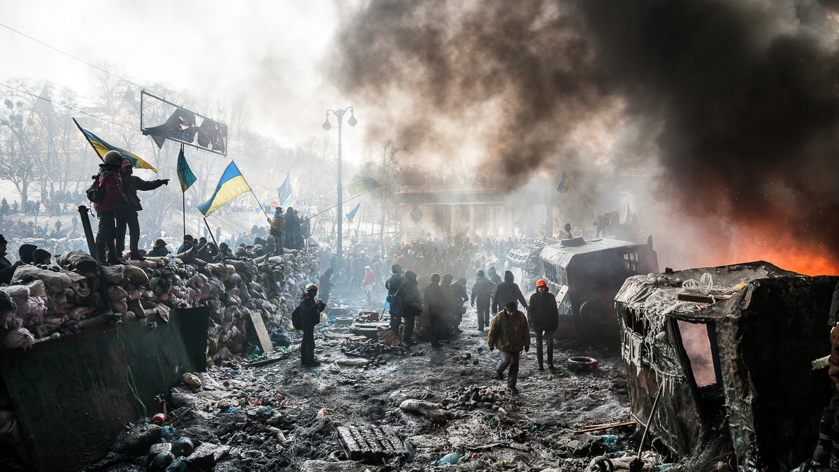 en grupp människor som håller i ukrainska flaggor, rök från brinnande barrikader,