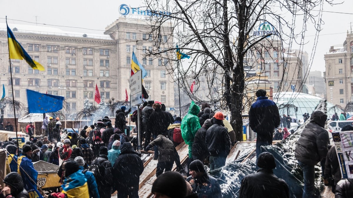 Människor står på ett torg, på högar av bråte. Husfasad i bakgrunden. Kiev, Ukraina, 2013.