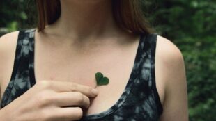 Ung kvinna håller ett hjärtformat blad över sitt eget hjärta.