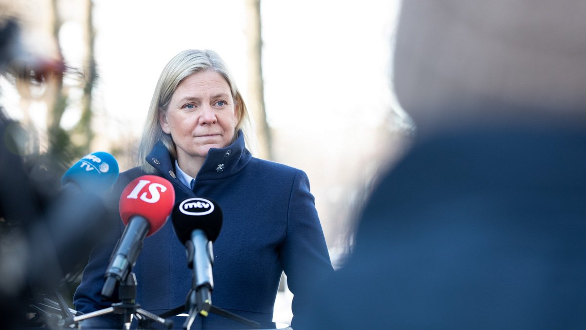 Magdalena Andersson i blå kappa bakom flera stora mikrofoner tittar uppmärksamt på frågeställare från finsk press.