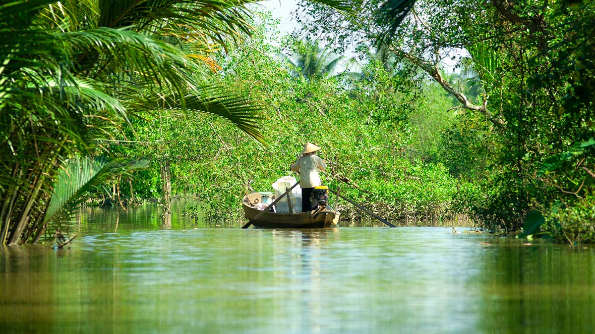 Man med båt på flod omgiven av tät växtlighet.