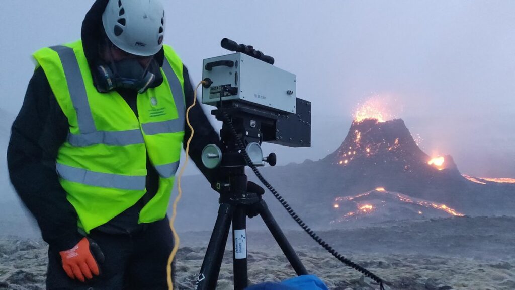 Forskare i skyddsutrusting，hjälm och reflectväst läser av mätutrustning i närheten av vulkanen。