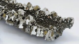 Silveraktiga metalliska kristaller i en klump, på vit bakgrund.