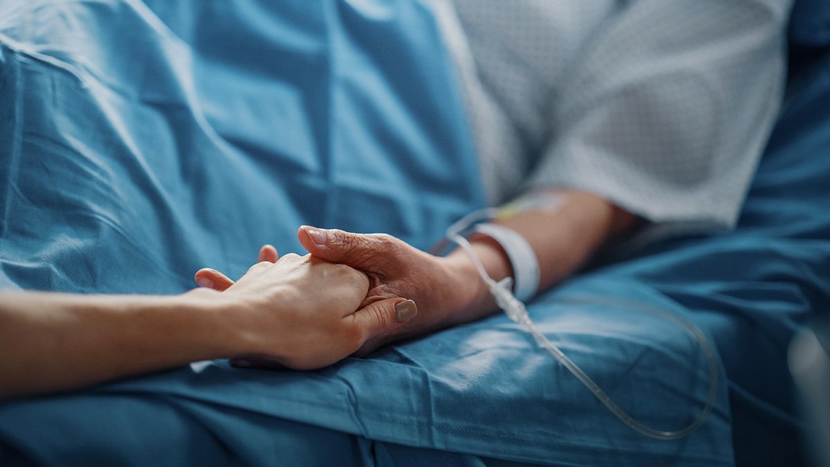 Sängliggande patient håller en person i handen.