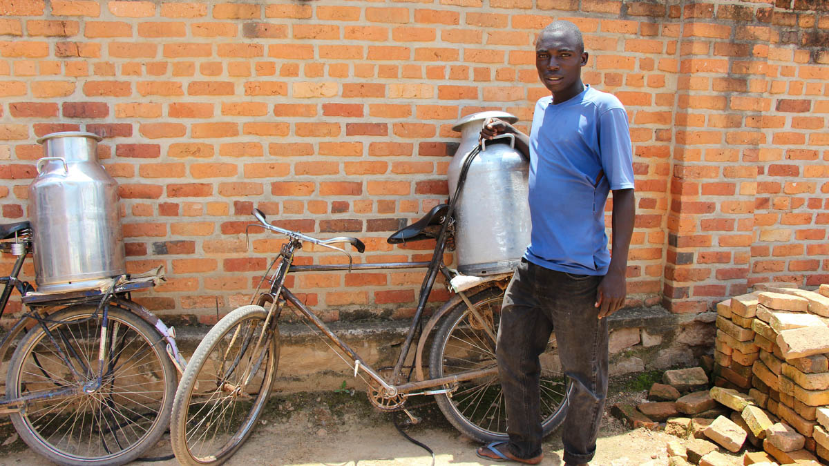 Man står brevid cykel lastad med stor mjölkkanna.
