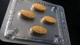 En grå läkemedelskarta med fyra bruna tabletter, mot mörk bakgrund.