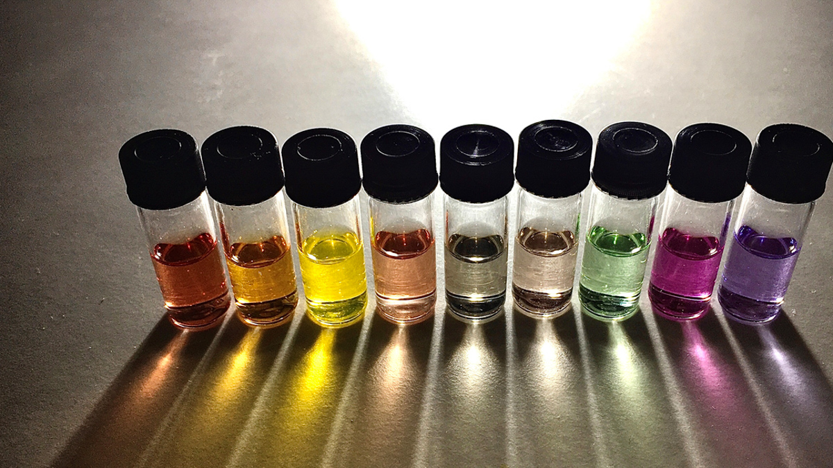 Nio små flaskor fyllda med vätska i olika färger.