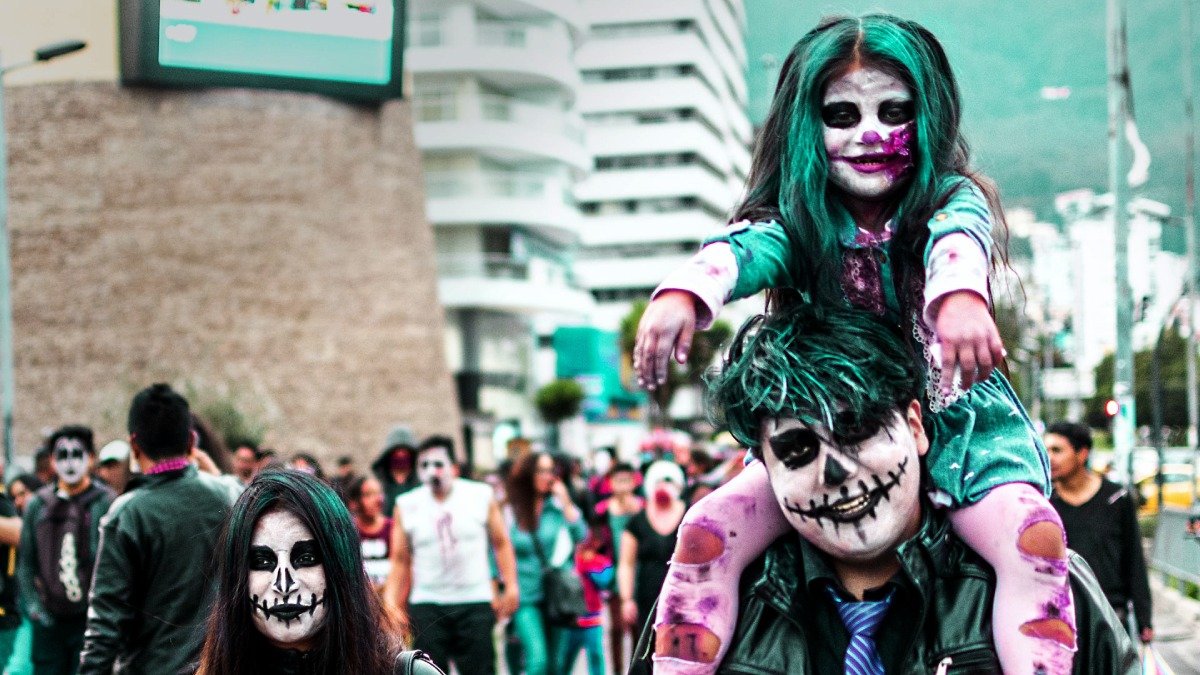 Två vuxna och ett barn, som sitter på den ene vuxnes axlar, sminkade till zombies på gata
