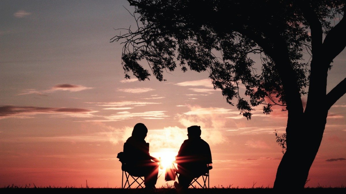 Två människor i svart siluett i solnedgång, invid träd