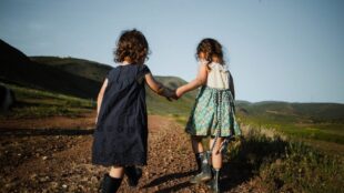 Två barn i femårsåldern går hand i hand på ett berg, sommar.