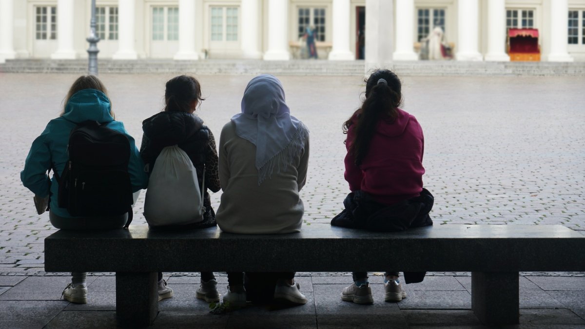 Fyra ungdomar på en bänk, med ryggen mot kameran, gammal byggnad framför dem.