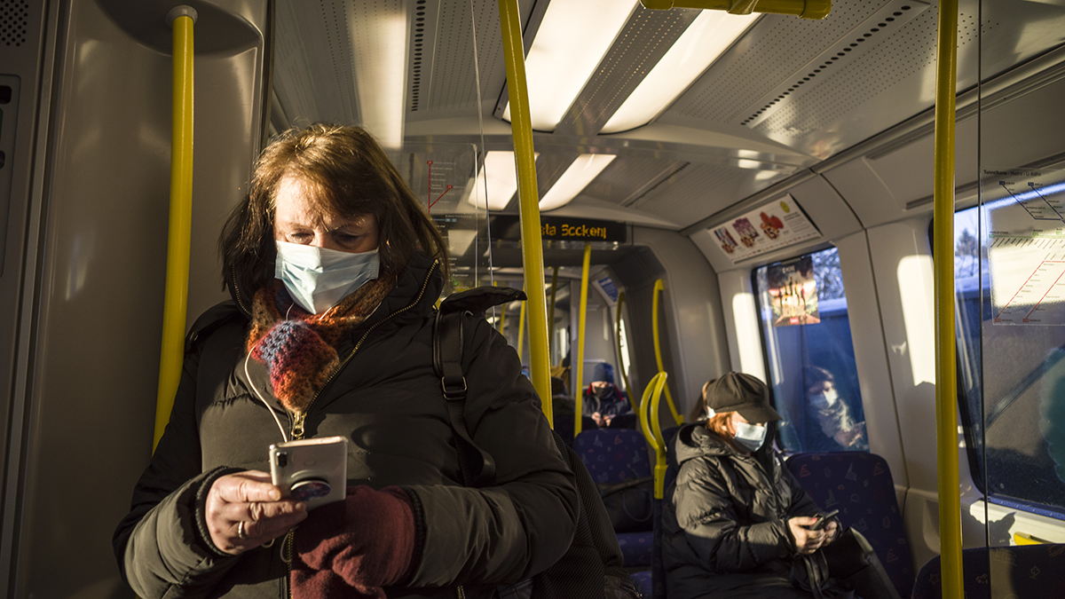 Kvinna åker buss med munskydd under coronapandemin och tittar på sin mobil.