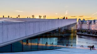 Stor byggnad med människor stående på den, solnedgång bakom, stadsmiljö. Oslo.