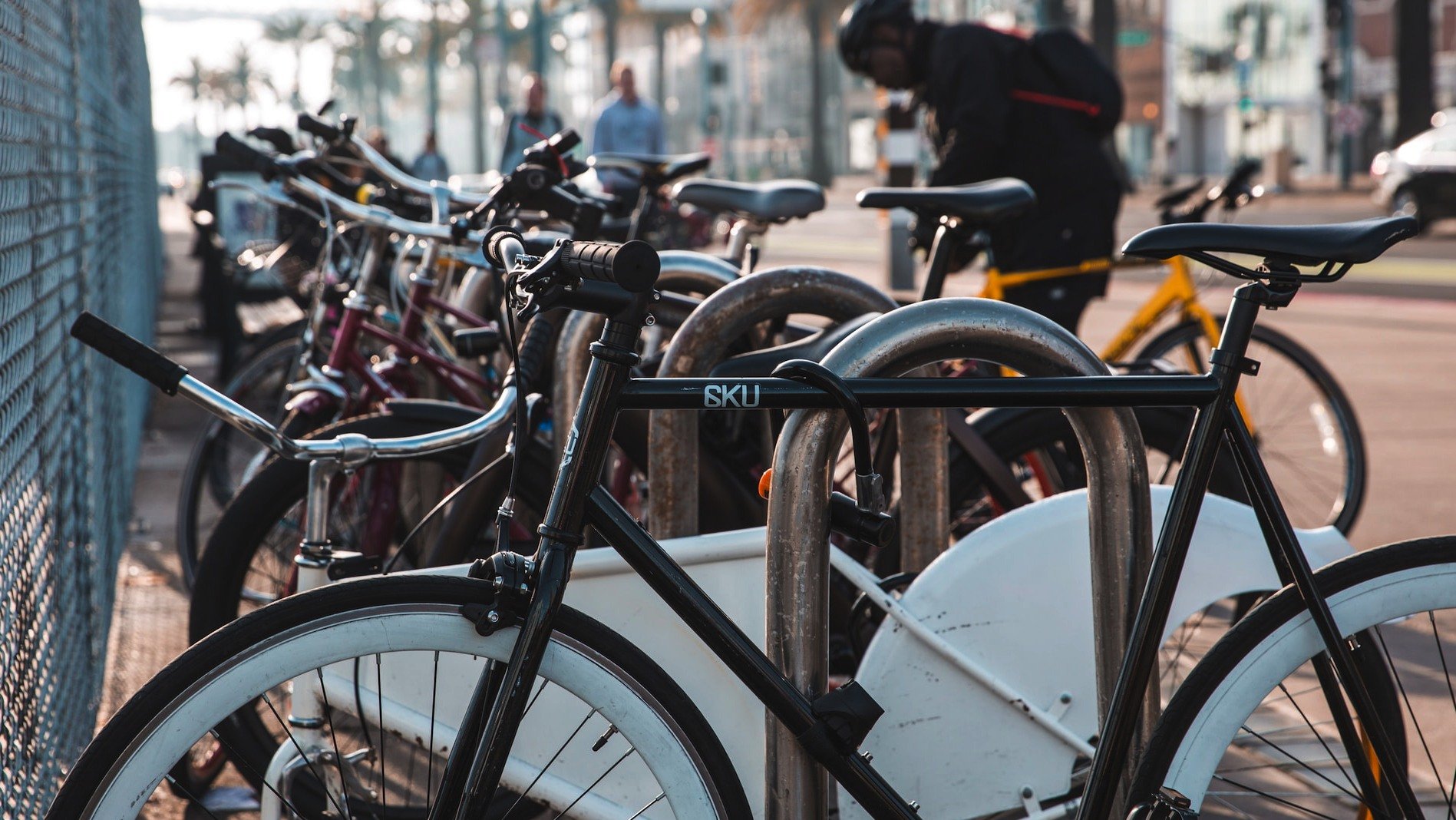 Problem med cykelstölder. Cykelställ med en rad låsta cyklar, cyklist i bakgrunden, stad.