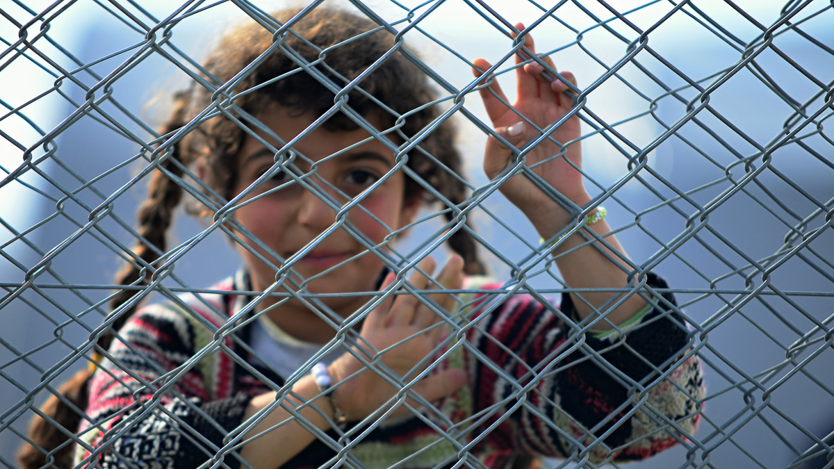leende flicka som står bakom nät i flyktingläger