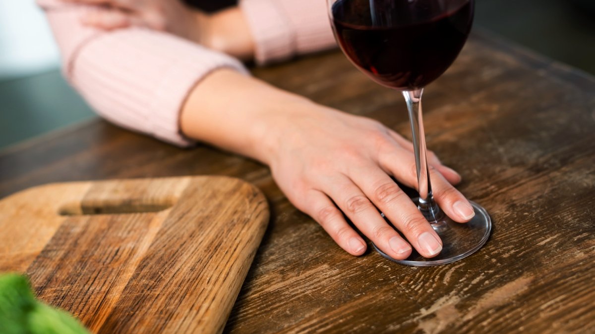 Hand på träbord håller om foten till ett glas rött vin.