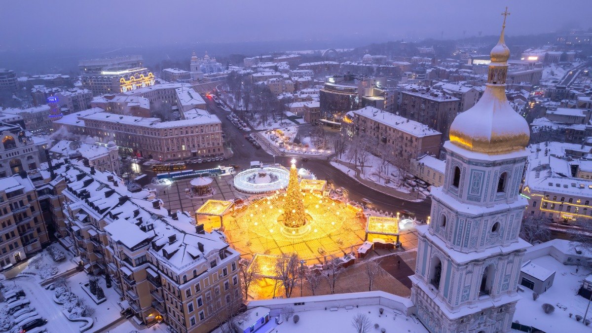 Stad sedd ovanifrån med snö på taken och torg med gul belysning.