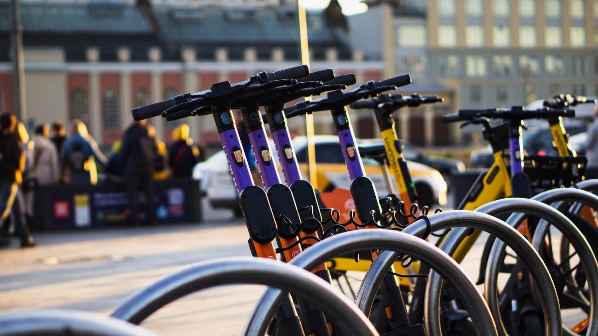 Parkerade elsparkcyklar i förgrunden, stadsmiljö med människor i bakgrunden