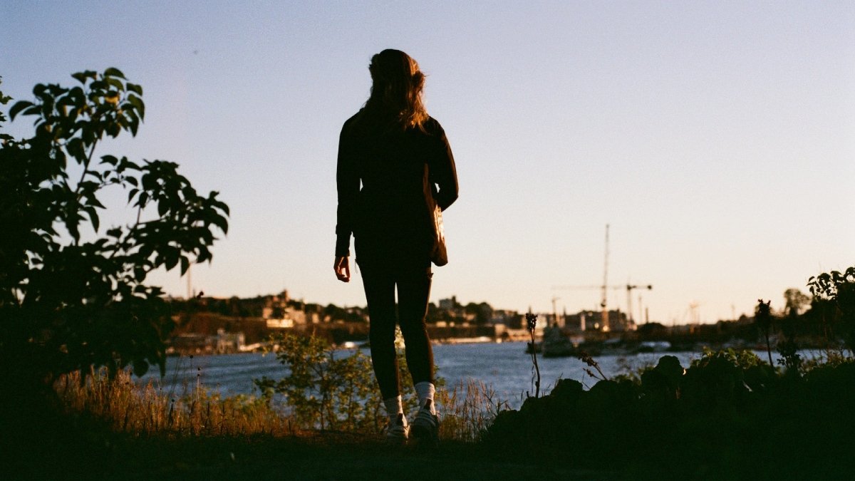 Kvinna i helfigur står och ser ut mot Stockholm, sedd bakifrån, sommartid.