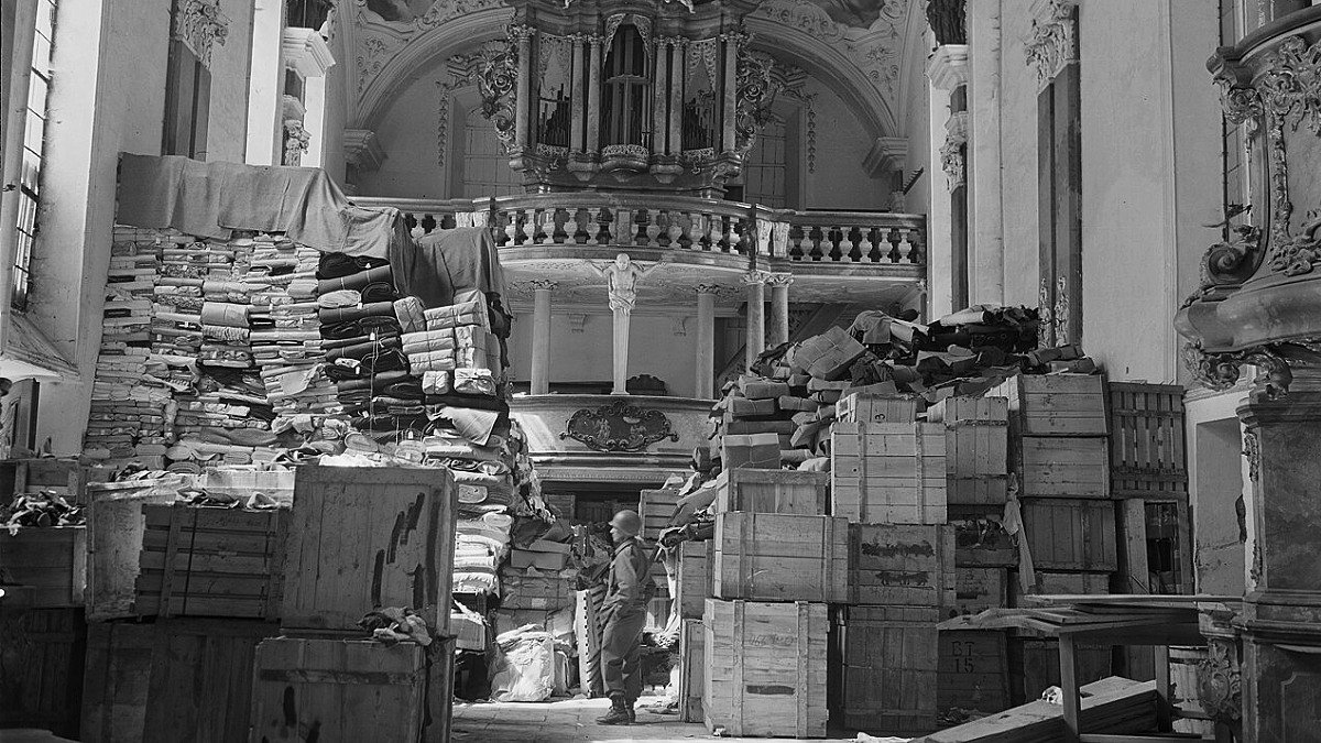 Svartvit bild av kyrka fylld med buntar av saker. Soldat på golvet.