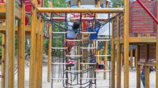 lekplats utomhus sommartid, två barn hänger från klätterställning.