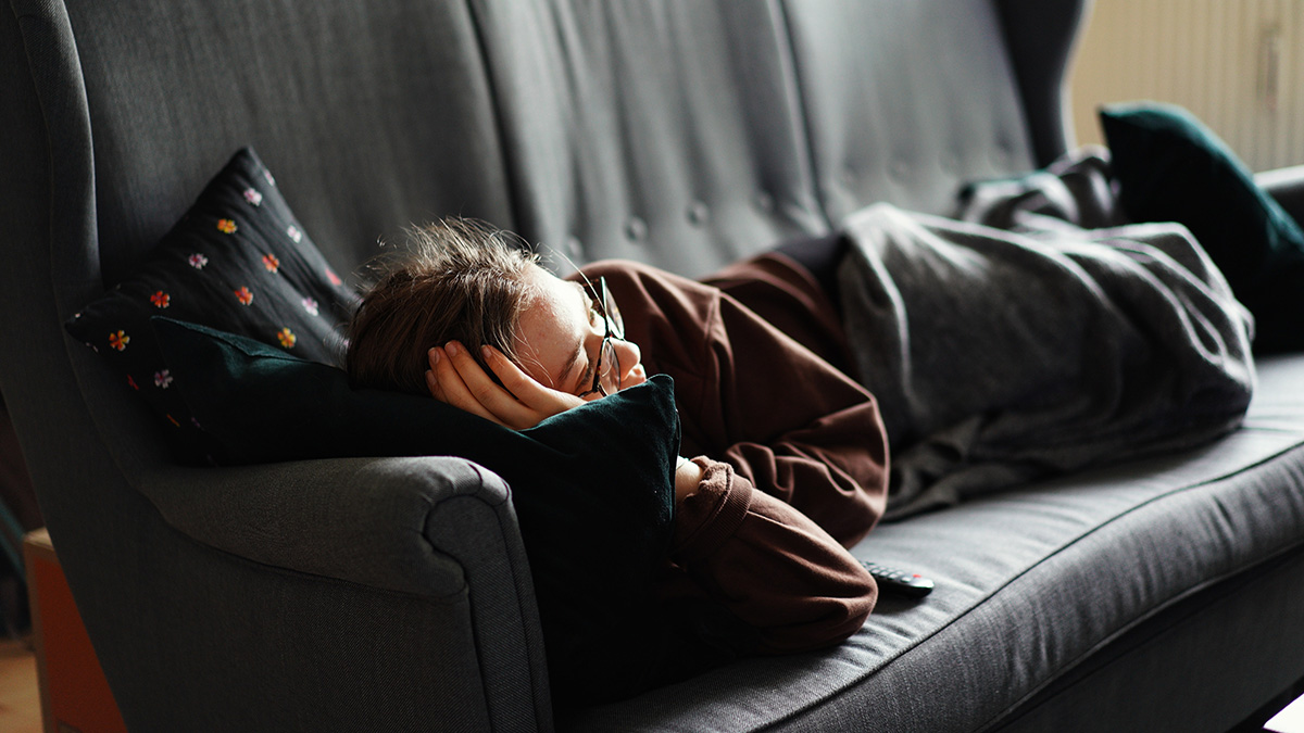 En människa ligger i en soffa under en filt och kollar på tv eller film.