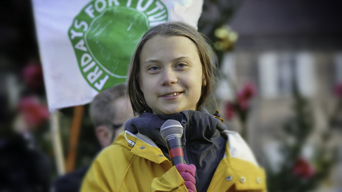 Greta Thunberg klädd i gul regnrock, håller i en mikrofon.