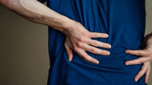En man i mörkblå tröja håller händerna på ryggen, i njurhöjd