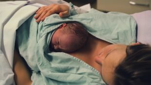En nyfödd ligger på bröstet, under en ljusgrön sjukhusrock.