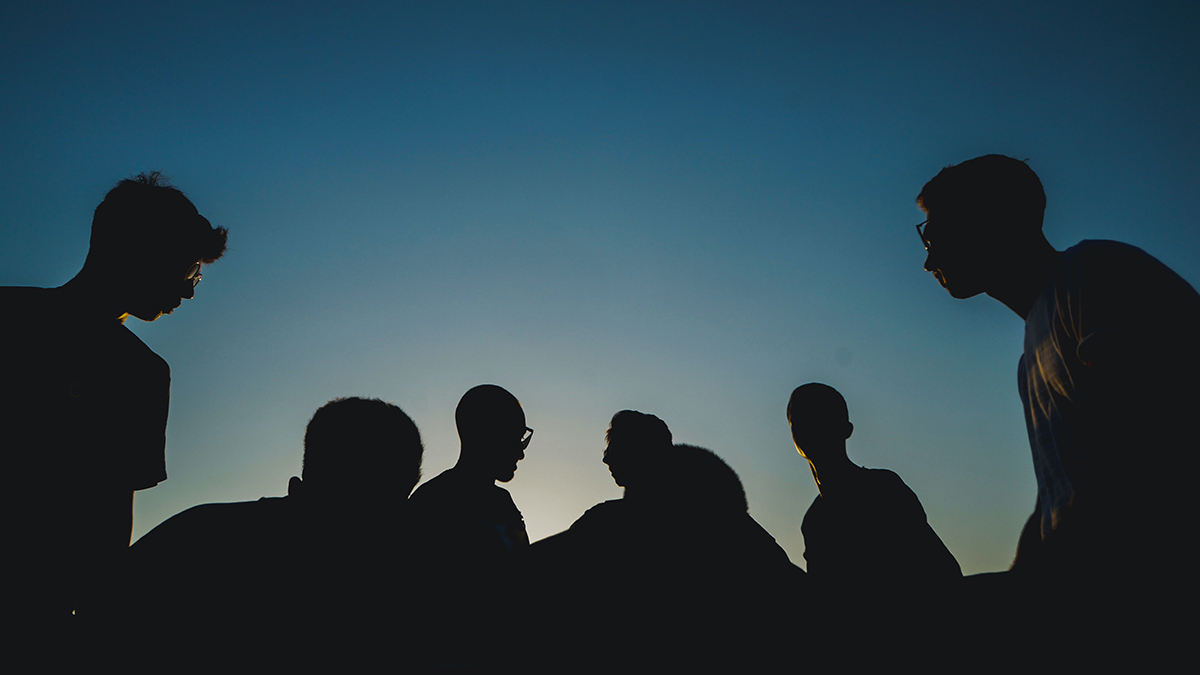 En grupp män avbildas som silhuetter mot en mörk himmel.