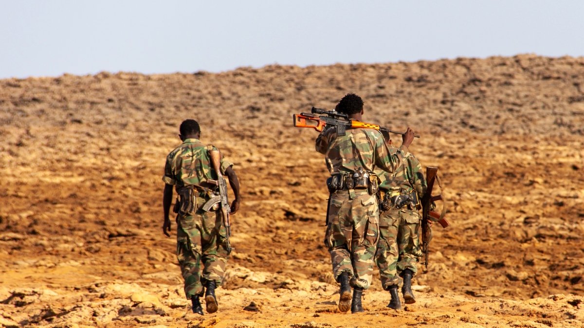 Tre soldater i kamouflagekläder går genom en öken, med ryggen mot kameran.