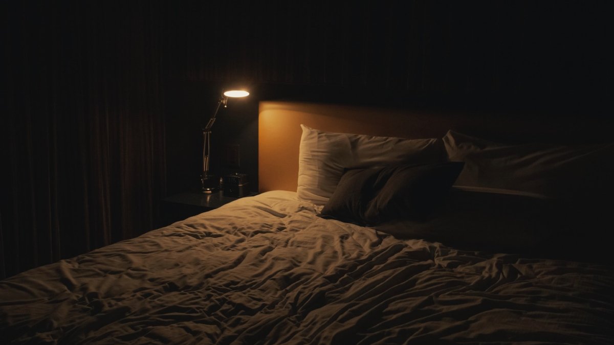 En tom säng i mörkret, med liten lysande sänglampa.