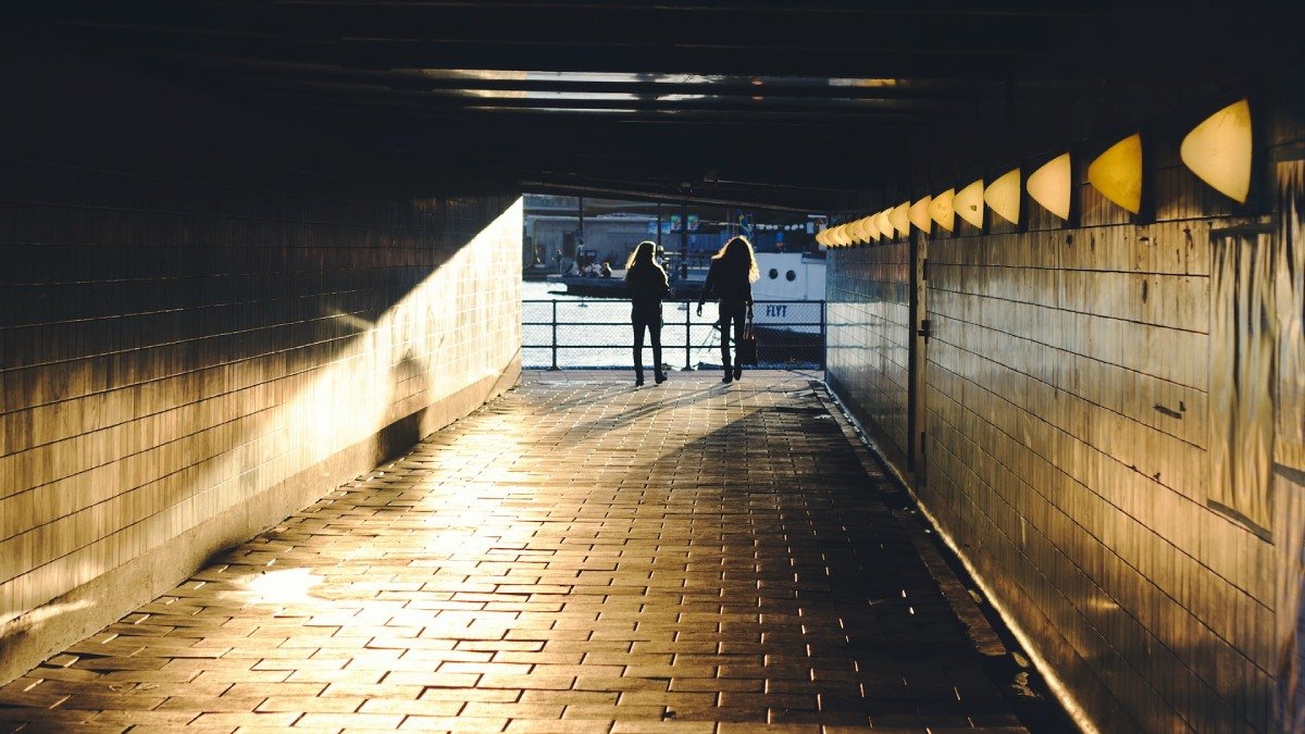 Tunnel, vid slutet ses två gående personer i siluett. Solen lyser in i tunneln, vatten framför personerna.