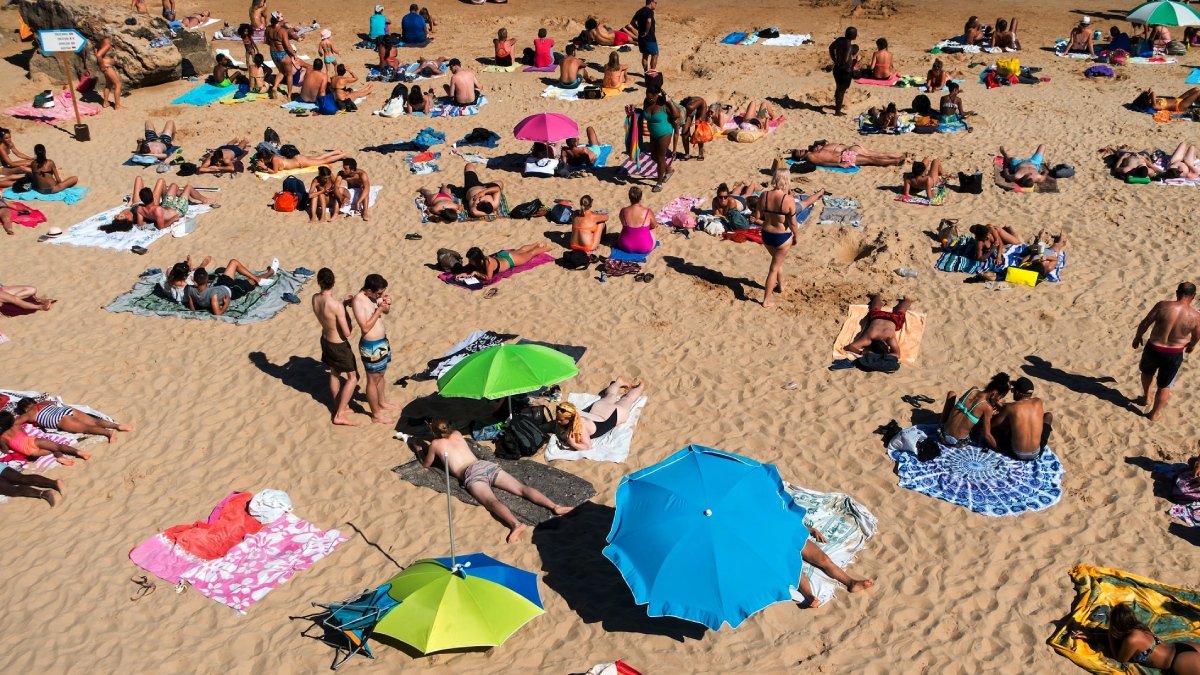 Sandstrand med parasoller och solbadare, sedd snett uppifrån.