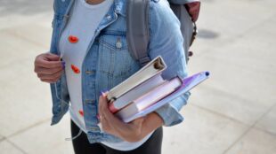 Att studera samma som föräldrarna är inte ovanligt. Här syns en person utomhus i vit tröja och jeansjacka med en bunt böcker under armen.