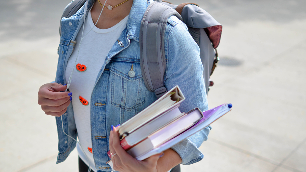 Student på högre utbildning som bär en trave böcker