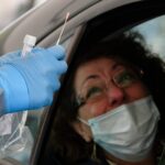 En person med gummihandskar håller fram ett testkit för covid-19 mot en kvinna i en bil.