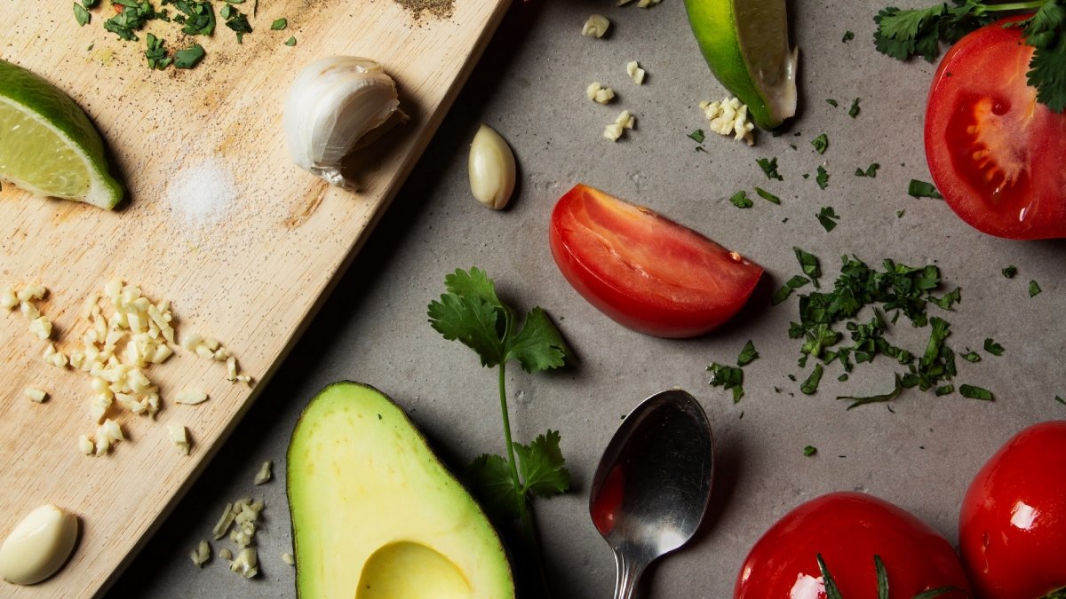 Skärbräda, bitar av vitlök, tomat och avocado på skärbrädan samt på bordet under.