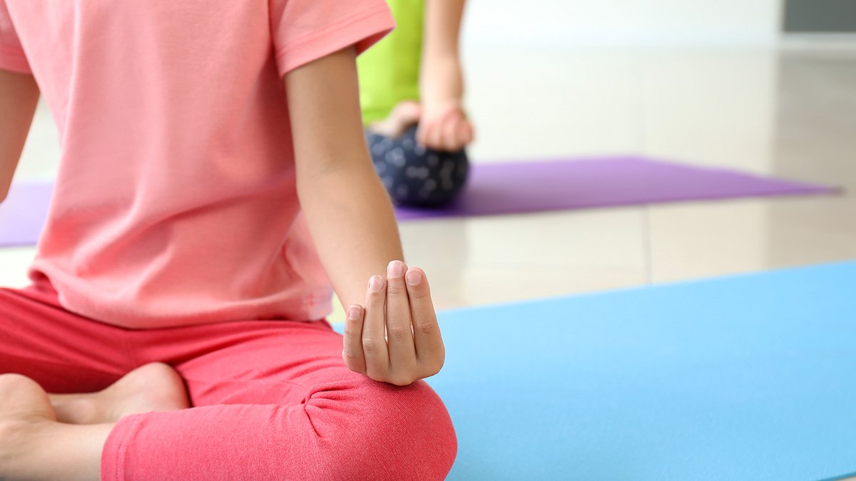 Flicka i rosa träningskläder sitter på yogamatta.