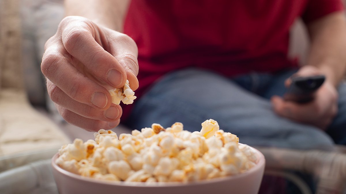 Man äter popcorn i tevesoffa.