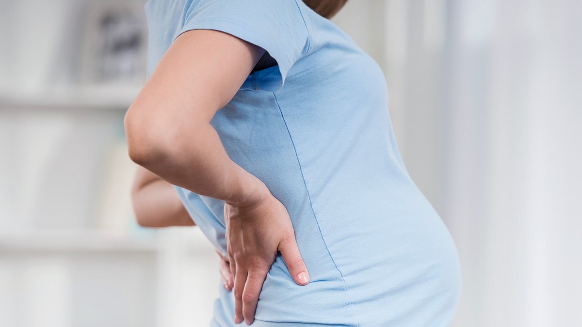 Gravid kvinna håller händerna i ryggslutet.